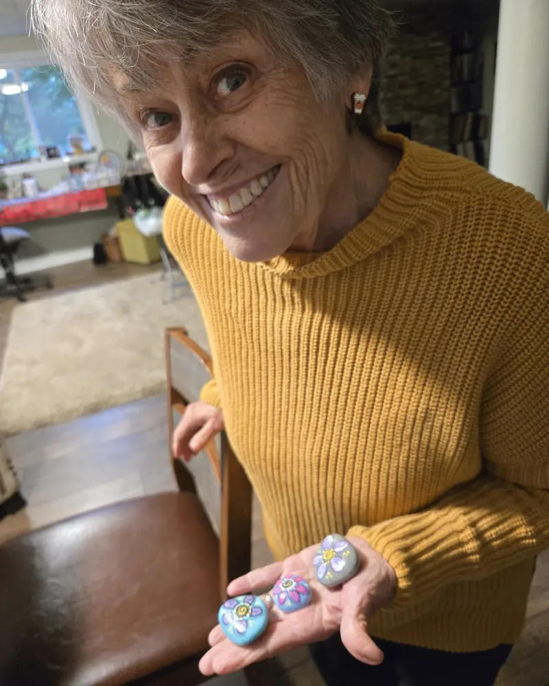 Susan Emmett smiling, holding three hand-painted flower stones